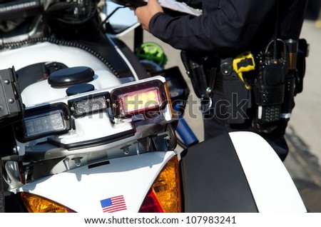a police officer writing a ticket next to his motorcycle during his shift.