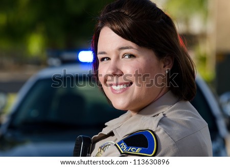 a female police officer smiles while standing in front of her patrol car.