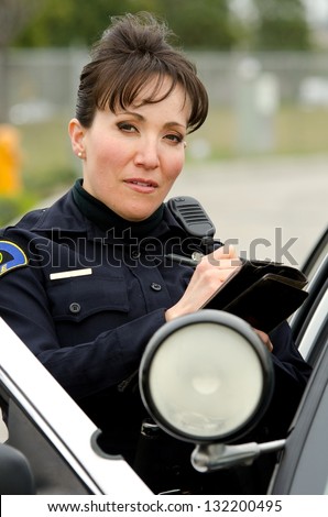 a female police officer standing next to her car as she writes a ticket.