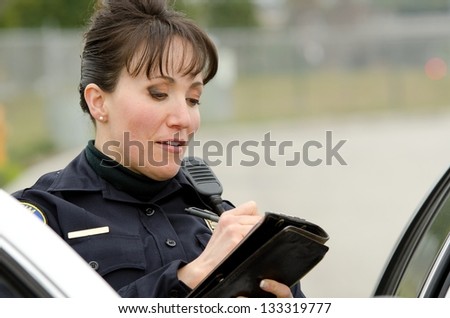 a female police officer writes a ticket while standing next to her patrol car.