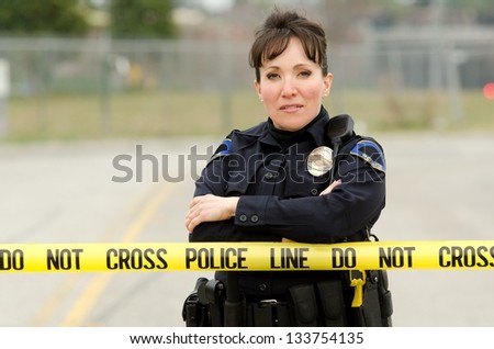A friendly looking female officer standing behind crime scene tape with her arms crossed.