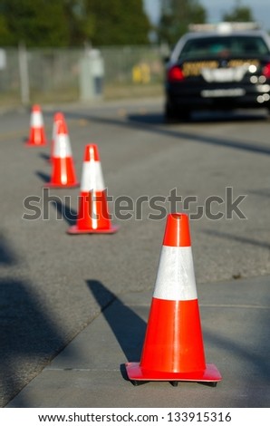 orange cones set up to direct traffic around a police car at a collision scene.
