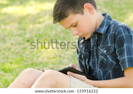 a 10 year old looking down and reading his tablet in the park.