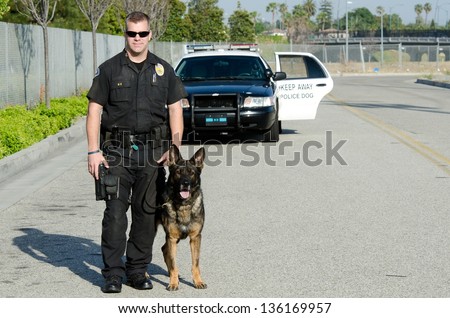 A K9 police officer standing with his partner with their patrol car in the background.