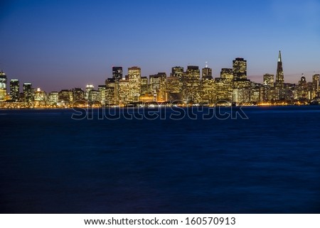 The city lights of San Francisco at twilight with the Bay Bridge on the left.