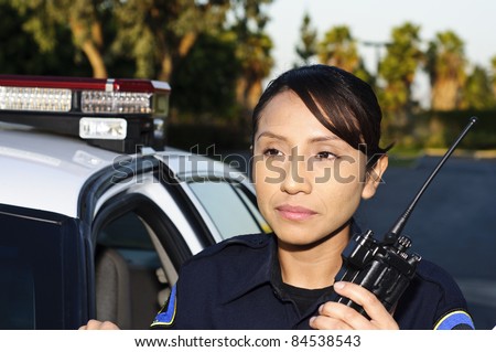 a female police officer standing next to her unit while she\'s about to talk on her radio.