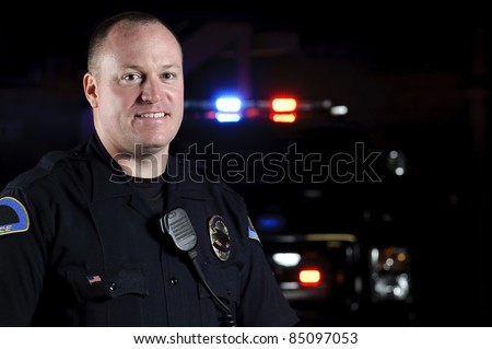 a smiling police officer in the night in front of his patrol unit.