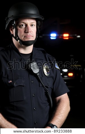 a police officer wearing a riot helmet with his patrol unit in the background.