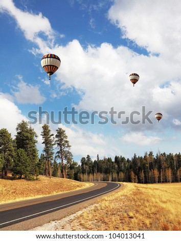 Huge balloons with a passenger basket fly over charming rural road