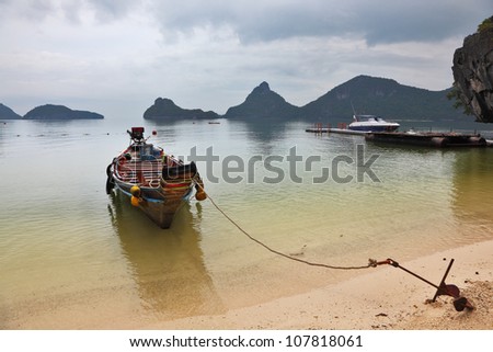 Thai Longtal boat moored on a sandy beach with an anchor. Picturesque bay on the island surrounded by islands