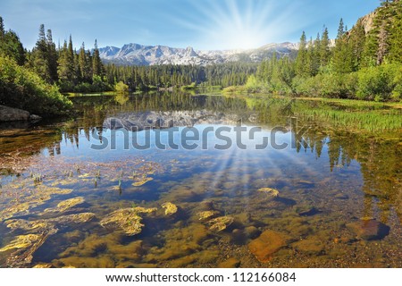 The magnificent mountains and northern sun are reflected in the smooth waters of a mountain lake