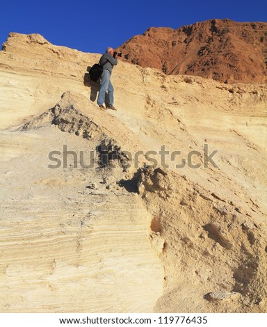 The gray-haired man photographs in a canyon at coast of the Dead Sea. On a shoulder at it a bag of the professional photographer.