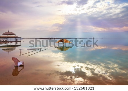 A stunning visual effect on the Dead Sea. The picturesque gazebo for bathers and sun rays are reflected in a smooth sea surface.