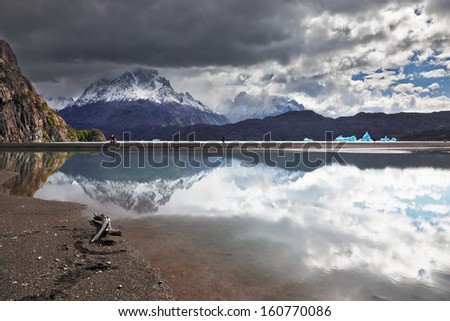 Iceberg in the lake. Bright reflections of sky and clouds in the smooth cold water of Lake Grey. Chilean Patagonia, National Park Torres del Paine