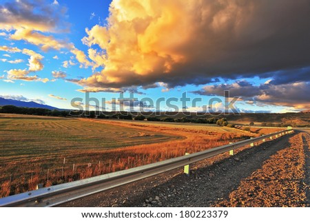 In the steppe runs a gravel road. Storm over the Pampas. The enormous storm cloud and a flat plain covered in orange sunset.