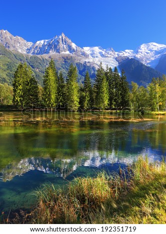 City park in the mountain resort of Chamonix in France. Snowy mountains and evergreen spruce reflected in the lake