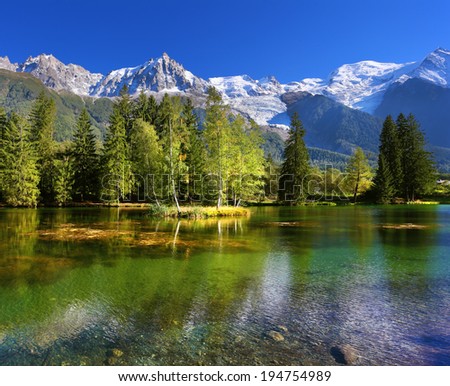 Cozy urban park in Chamonix. Snowy Alps picturesquely surrounded by evergreen trees and lake