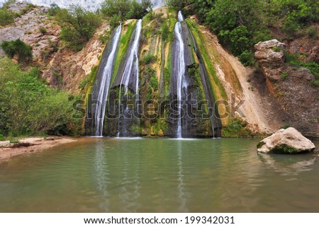 Three-jet scenic waterfall in the mountains. Three parallel streams of water running down the steep slope and fall in oval pool