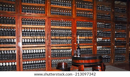 MADEIRA, PORTUGAL - OCTOBER 8, 2011: Wooden shelves with bottles of wine. Storage space for expensive aged wines - Madeira. Round table with  bottle, which is inserted the candle