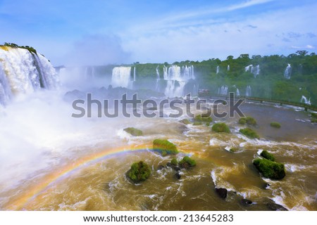 White whipped foam of water and a thin mist over the water.  Magnificent rainbow shines in the mist. The most high-water waterfall in the world - Iguazu. The Brazilian side of the park.