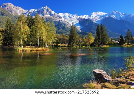 Lake with cold water surrounded by trees and snow-capped mountains. City park in the Alpine resort of Chamonix