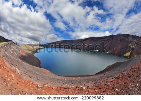 Iceland in July. Oval blue lake in the crater of the volcano cooled down. Steep banks of the lake of red rhyolite