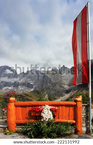 The small picturesque fence cozy cafe in the Austrian Alps. The short fence decorated with flowers. Near the flagpole installed in the Austrian flag