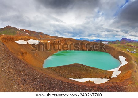 July in Iceland. Lake in the crater of an extinct volcano. Lake water bright green color. On the shores lie snowfields from last year