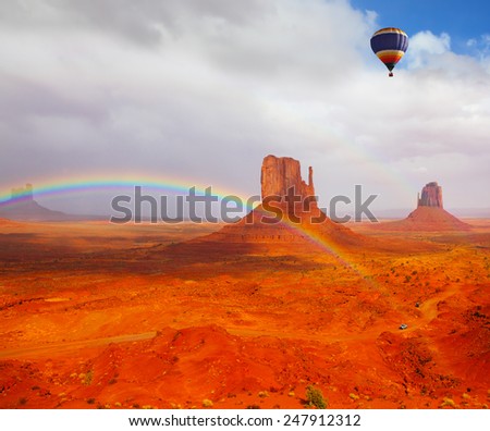 Huge balloon flies over Red Desert Navajo, USA. The picturesque rainbow crosses some rocks - \
