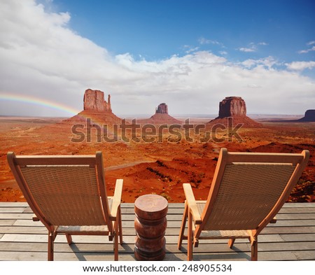 Red sandstone in the valley of the Navajo. Famous rock - mitts crosses the rainbow. Two chairs - deck chairs on the wooden platform are for tourists