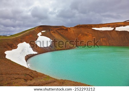 Picturesque Krafla lake in the crater of an extinct volcano. Lake water bright green color. On the shores lie snowfields from last year