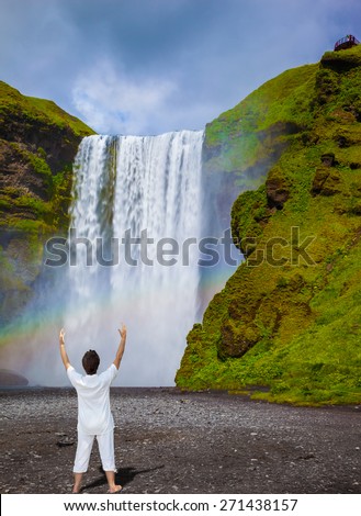 Grand waterfall with rainbow in the water mist Skogafoss. Elderly woman shocked by the beauty of the waterfall