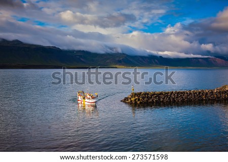 White fishing boat in the harbor pier fishing village Arnastapi. Sunset on the sea fjord in Iceland