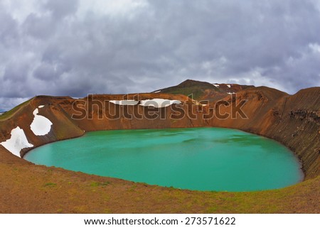 Picturesque Krafla  lake in the crater of an extinct volcano. Lake water bright green color. On the shores lie snowfields from last year