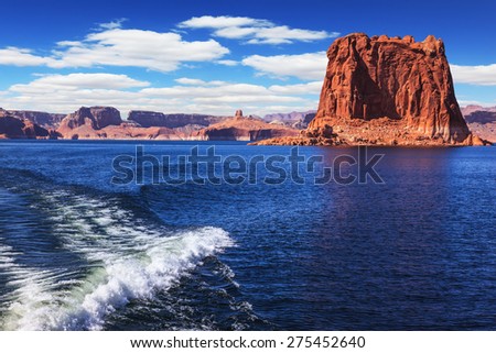 Foamy trace of a motor boat crosses the emerald waters. In the distance the coast of red sandstone. Lake Powell on the Colorado River