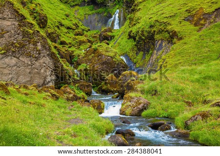 July in Iceland. Basalt mountains overgrown with a green grass and moss. Picturesque cascade step falls