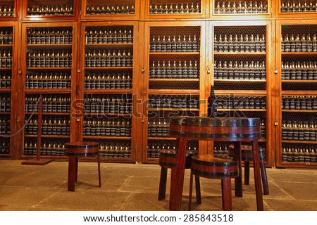 FUNCHAL, MADEIRA - OCTOBER 08, 2011: Museum - repository of expensive vintage wine Madera. Long rows of shelves made of bottles of wine. In the aisle is a round table and stools