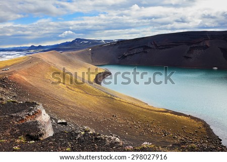 Iceland in July. Oval blue lake in the crater of the volcano cooled down. The lake shores are made of rhyolite
