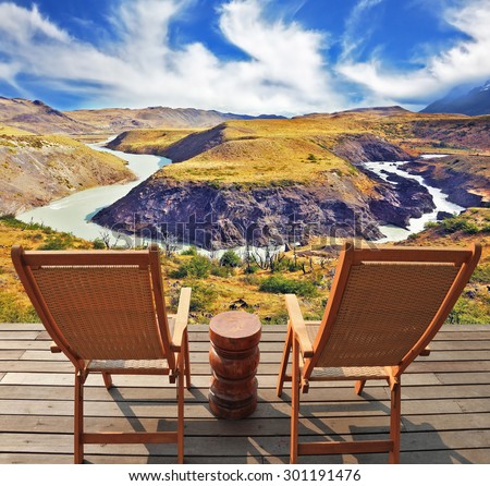 Two wooden chairs - on a wooden platform.  The comfortable place to enjoy the beauty of the landscape. The magnificent park Torres del Paine in Chile.  Picturesque river bends a horseshoe of hills.