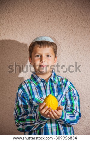 The etrog - ritual fruit for Jewish holiday of Sukkot. The charming seven-year-old boy in white festive skullcap holds citrus in hand