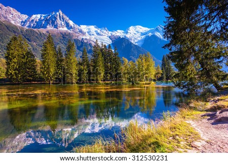 The snow-covered Alps and evergreen fir-trees  reflected in lake. Early fall in Chamonix, Haute-Savoie