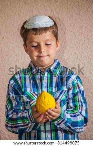 Etrog -  ritual fruit for the Jewish holiday of Sukkot. Beautiful seven year old boy in white knitted skullcap is holding citron