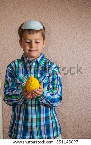 Etrog -  ritual fruit for the Jewish holiday of Sukkot. Beautiful seven year old boy in white knitted skullcap is holding citrus