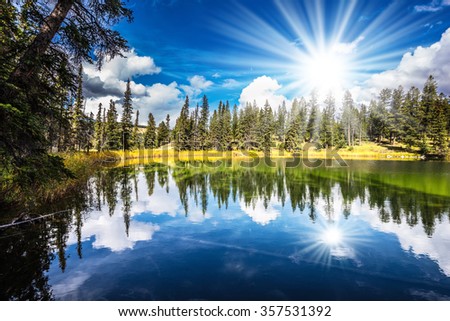 Jasper National Park in the Rocky Mountains of Canada. A great morning sun is reflected in smooth water of the lake. On shores of the lake grow coniferous forests
