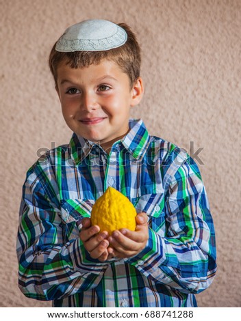 Citron - ritual fruit for the Jewish holiday of Sukkot. Beautiful seven year old boy in white knitted skullcap is holding citrus