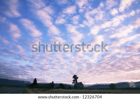Pink clouds in the evening sky above the rural house near to road