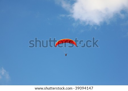 The operated red parachute flies in high in the blue sky