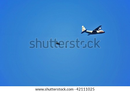 The military plane and a parachute with the parachuter in the dark blue sky above quay of Tel Aviv