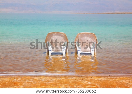 Two white beach chairs stood side by side in the water at the beach. Dead Sea, Israel
