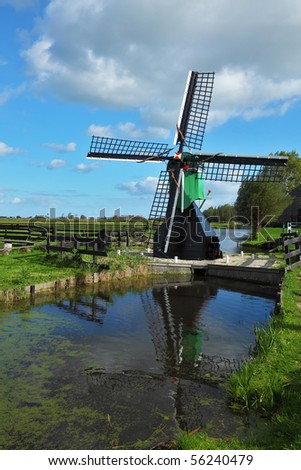 The ancient windmill is reflected in water of a small pond. Clear autumn day in the Netherlands
